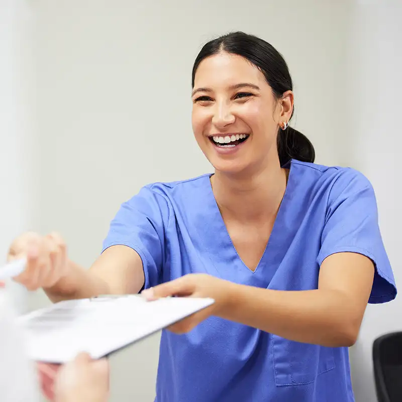 Smiling dental staff holding out clipboard to patient