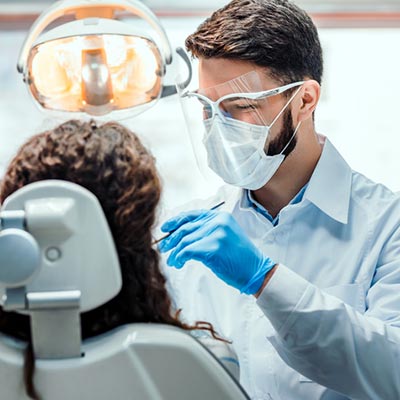 Dentist wearing a face shield and face mask performs a dental procedure on a patient