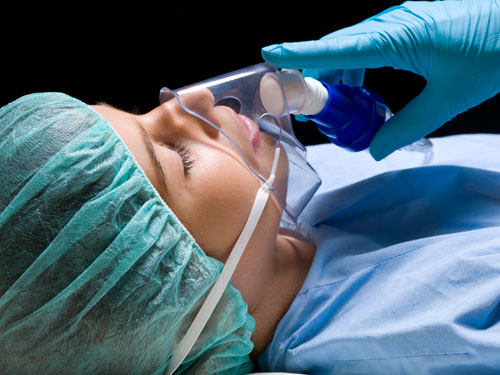 gloved hand holds breathing mask to sleeping patient's face