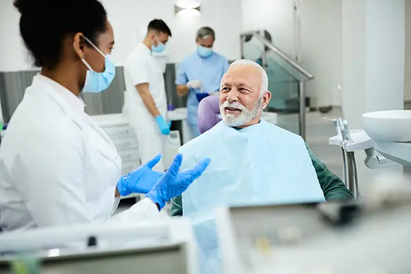 Older patient sitting in dental chair calmly discussing his medications with female dentist at Mountain State Oral and Facial Surgery in Charleston, WV