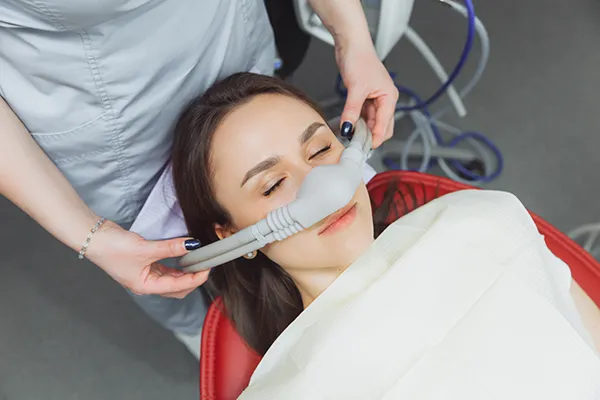 Dental assistant fitting a sedation mask over the nose of her calm female patient at Mountain State Oral and Facial Surgery in Charleston, WV